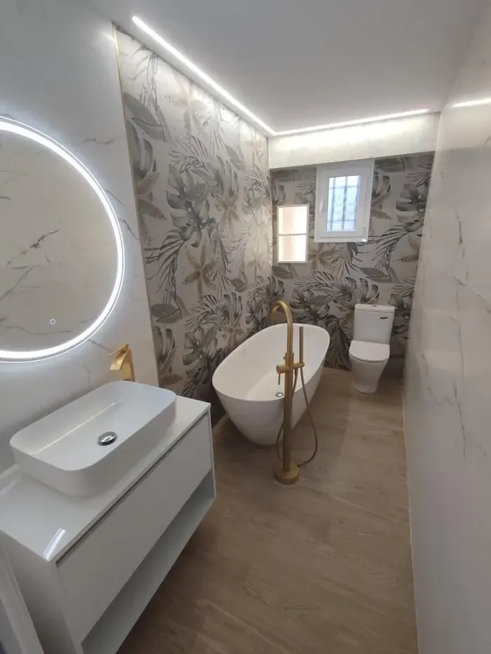 Baño con bañera exenta, grifería dorada y papel pintado de hojas