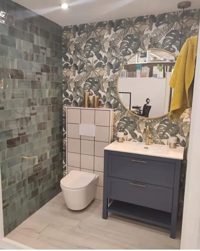 Baño con papel pintado tropical, azulejo verde y mueble azul