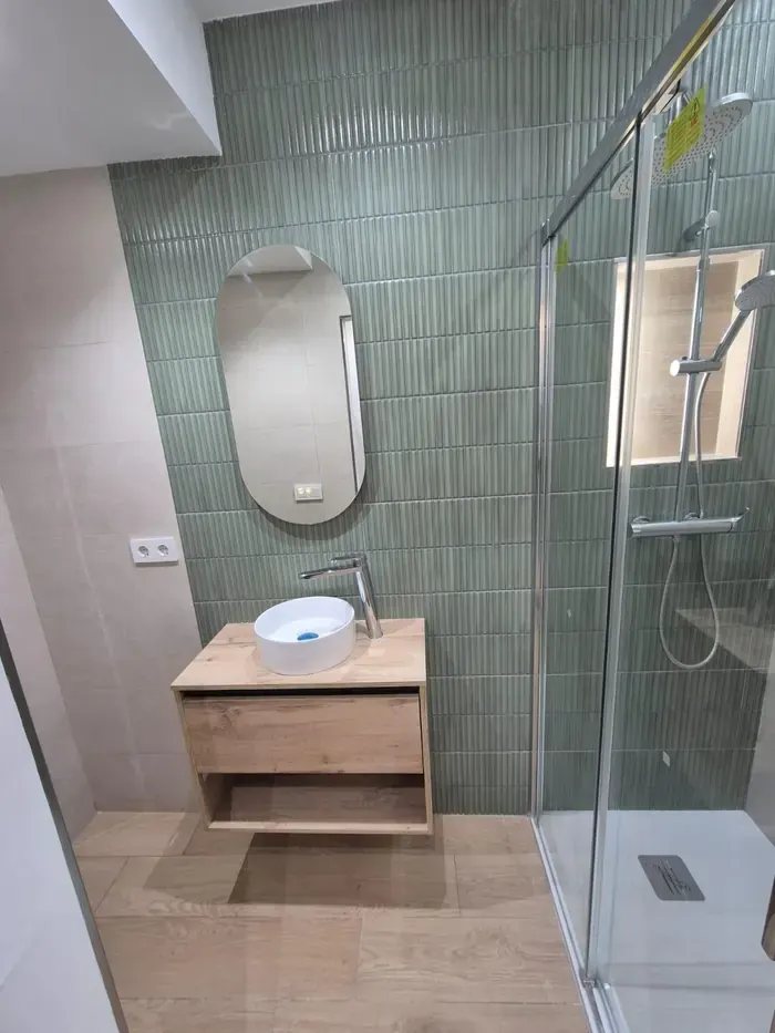Baño con azulejo vertical verde, espejo ovalado y mueble de roble