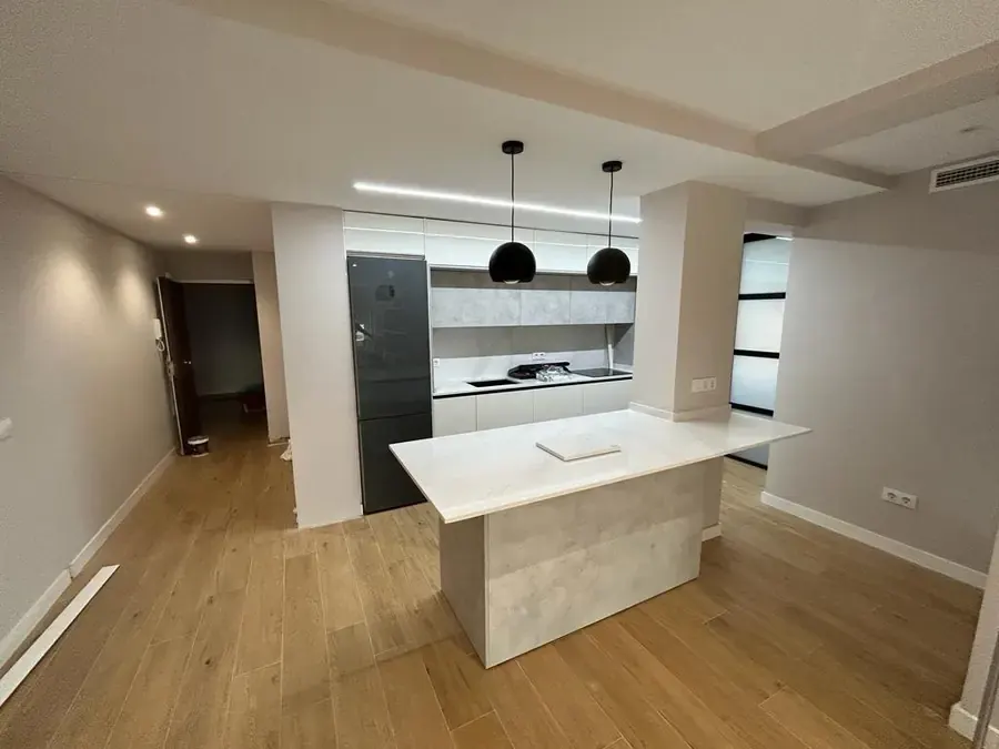 Cocina con isla de encimera blanca y dos lámparas negras colgantes