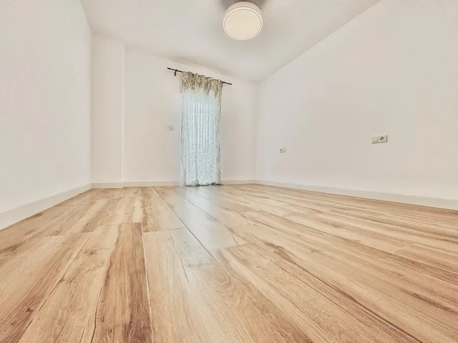 Habitación vacía recién terminada con suelo de madera clara y paredes blancas