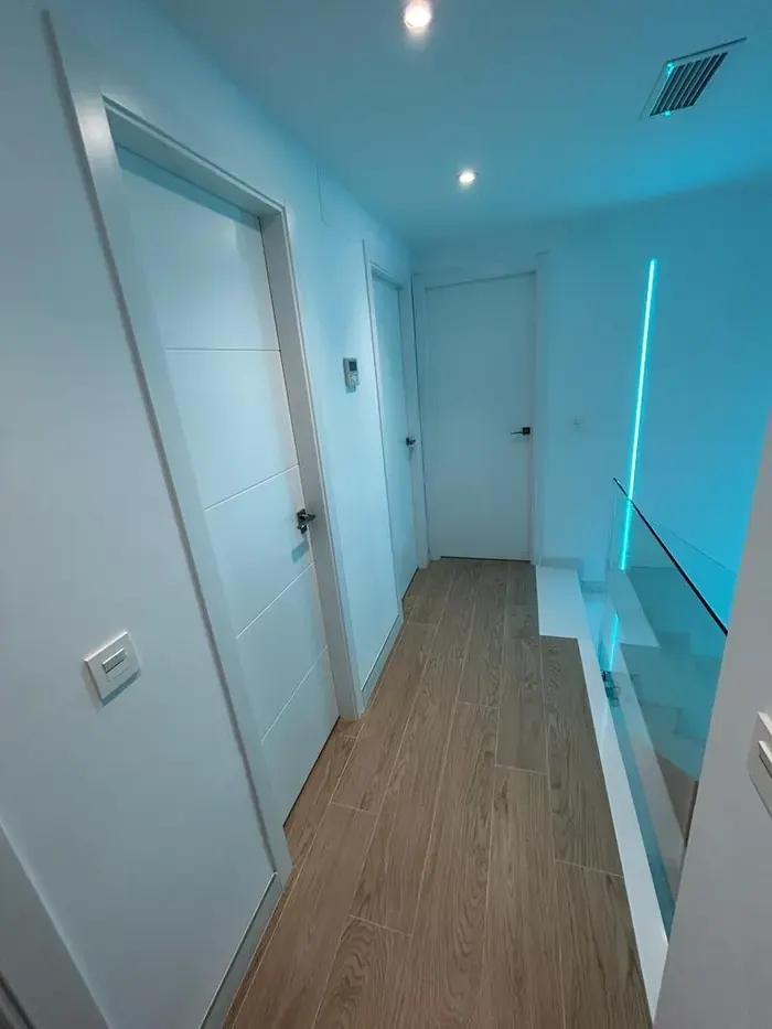 Pasillo con puertas blancas, barandilla de cristal y tiras de luz LED en el techo