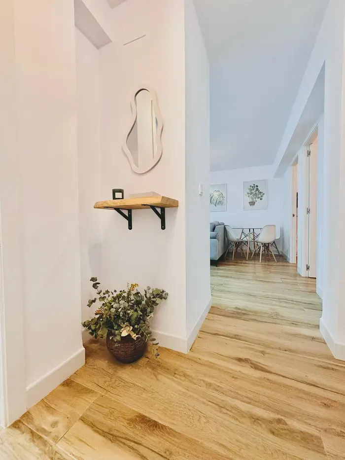 Pasillo blanco con suelo de madera, balda y espejo ondulado